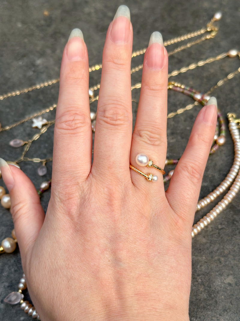 Hand wearing a gold ring with pearls against a textured surface
